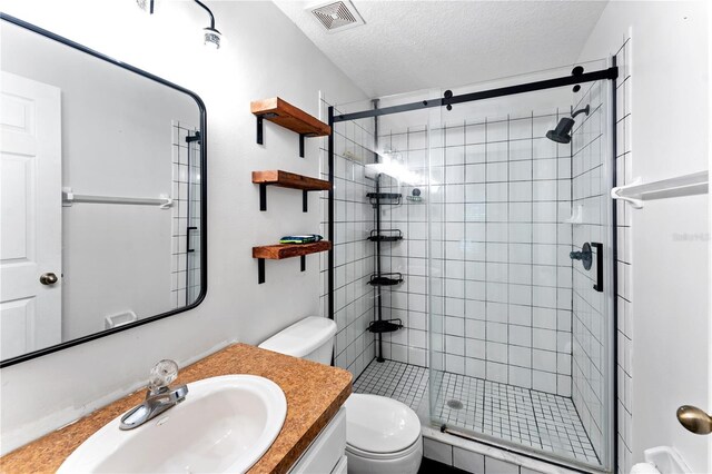 bathroom with a shower with door, a textured ceiling, vanity, and toilet