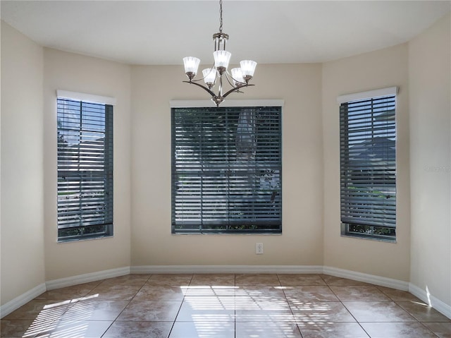 unfurnished dining area featuring a notable chandelier, baseboards, and tile patterned floors