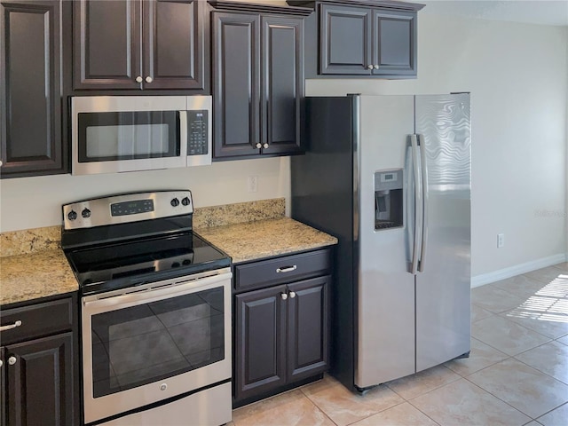 kitchen featuring baseboards, appliances with stainless steel finishes, light stone counters, and light tile patterned flooring