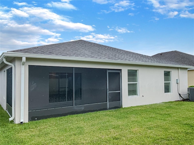 rear view of house with central air condition unit, a sunroom, a yard, roof with shingles, and stucco siding