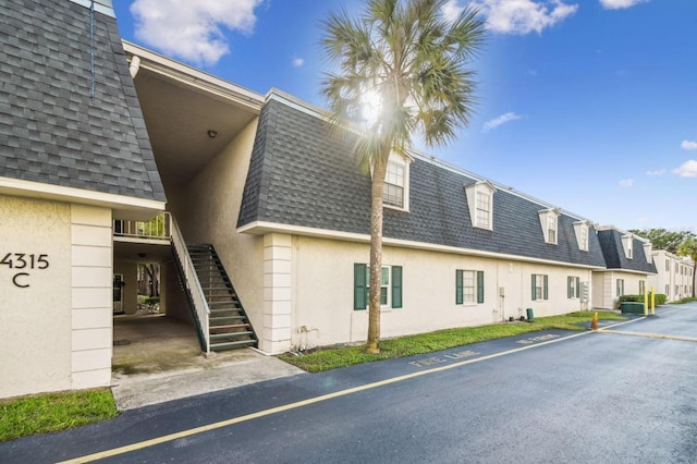 4335 Aegean Dr Unit 106A, Tampa, FL 33611 - view of side of property featuring mansard roof, a shingled roof, and stucco siding