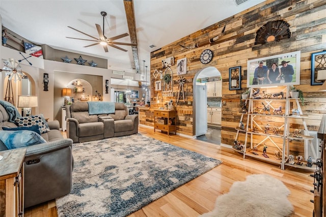 living room featuring ceiling fan, a towering ceiling, light hardwood / wood-style flooring, and wooden walls