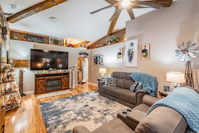 living room with a textured ceiling, ceiling fan, light hardwood / wood-style floors, and beamed ceiling