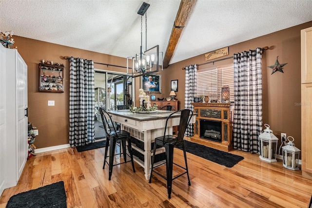 dining room with light hardwood / wood-style floors, beam ceiling, an inviting chandelier, and a textured ceiling