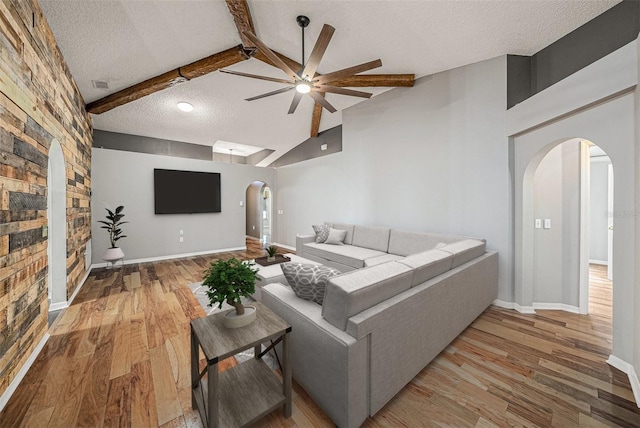 living area with arched walkways, a textured ceiling, wood finished floors, a ceiling fan, and beam ceiling