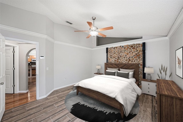 bedroom featuring arched walkways, ceiling fan, wood finished floors, vaulted ceiling, and a textured ceiling