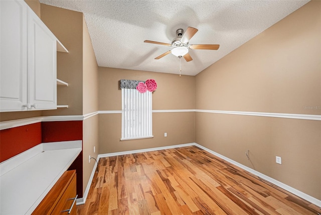 spare room featuring a textured ceiling, baseboards, light wood-style flooring, and a ceiling fan