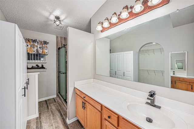 full bathroom featuring a textured ceiling, vanity, baseboards, wood tiled floor, and a stall shower