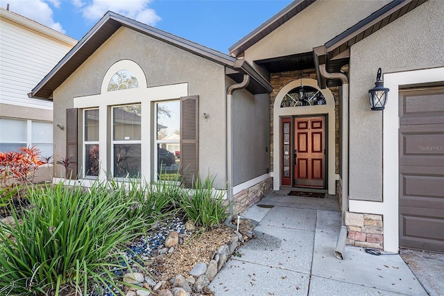 doorway to property featuring a garage, stone siding, and stucco siding