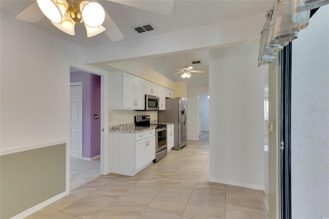 kitchen with ceiling fan, white cabinetry, appliances with stainless steel finishes, light stone countertops, and light tile patterned floors