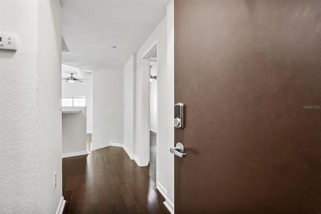 hall featuring a textured wall, baseboards, and dark wood-style floors
