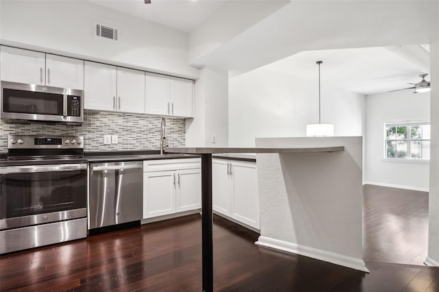 kitchen with ceiling fan, appliances with stainless steel finishes, kitchen peninsula, dark wood-type flooring, and pendant lighting