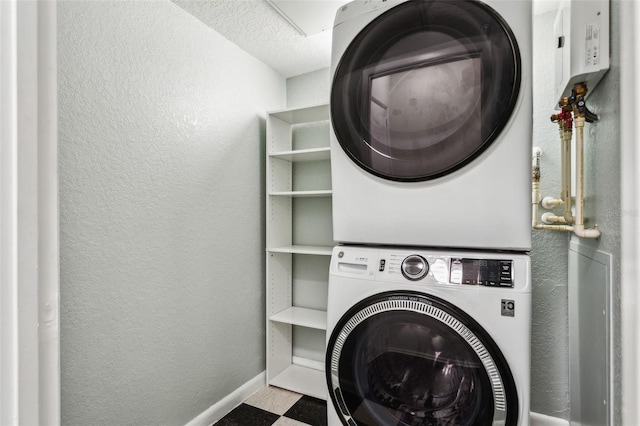washroom featuring baseboards, stacked washer and dryer, laundry area, and a textured wall