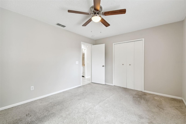 unfurnished bedroom featuring a closet, a textured ceiling, light carpet, and ceiling fan