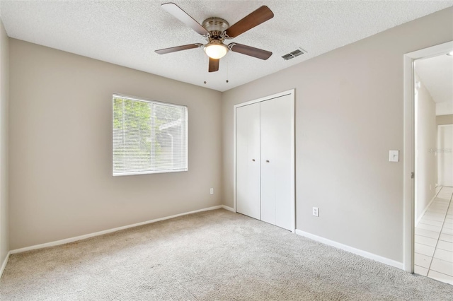 unfurnished bedroom featuring a closet, a textured ceiling, light carpet, and ceiling fan