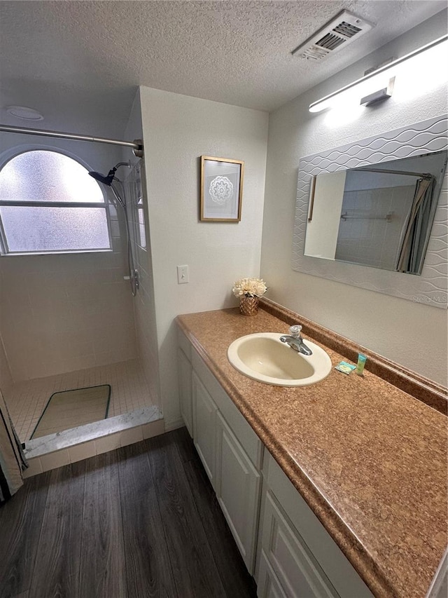 bathroom featuring vanity, a textured ceiling, a tile shower, and hardwood / wood-style floors