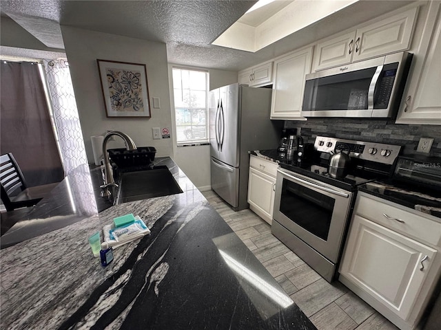 kitchen featuring backsplash, stainless steel appliances, white cabinetry, and a textured ceiling