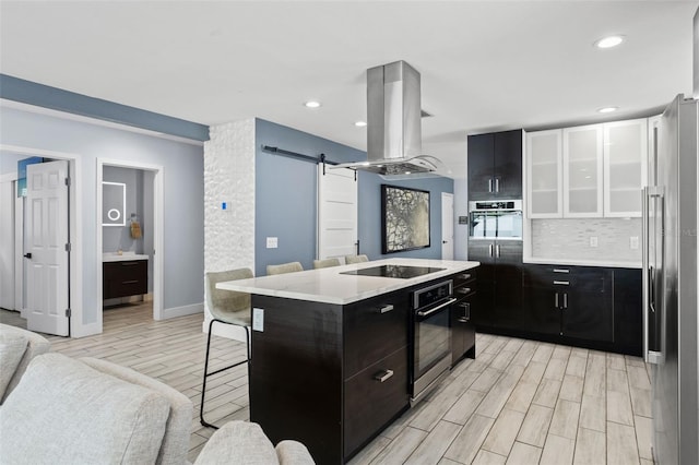 kitchen featuring island exhaust hood, light hardwood / wood-style flooring, stainless steel appliances, a center island, and a barn door