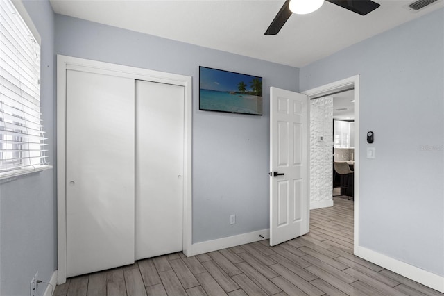 unfurnished bedroom with light wood-type flooring, ceiling fan, multiple windows, and a closet