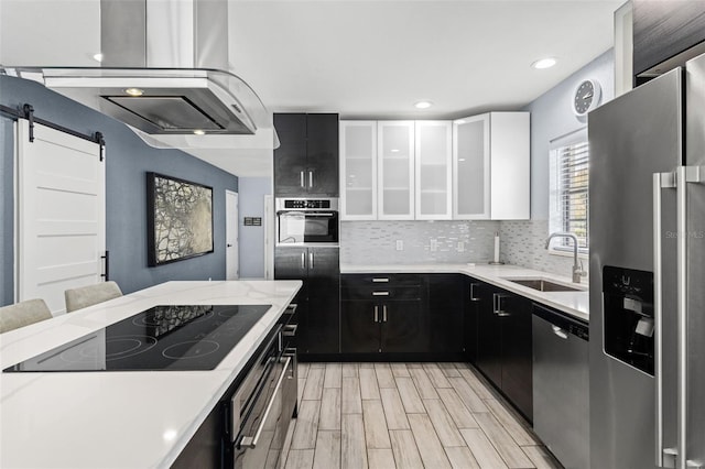 kitchen with white cabinets, sink, stainless steel appliances, a barn door, and light hardwood / wood-style floors