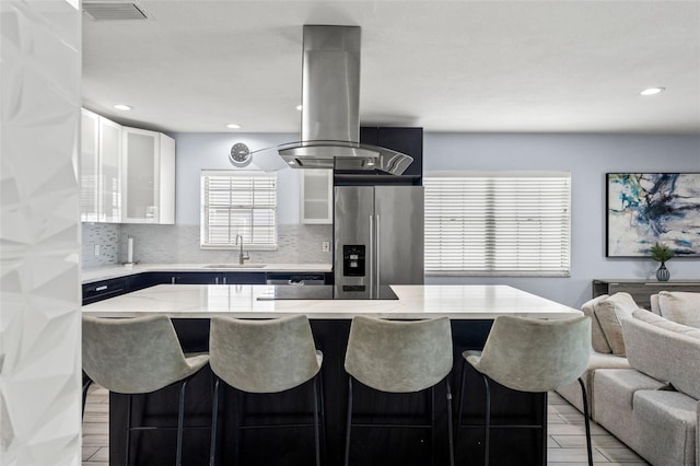 kitchen featuring stainless steel fridge, decorative backsplash, white cabinetry, a center island, and sink