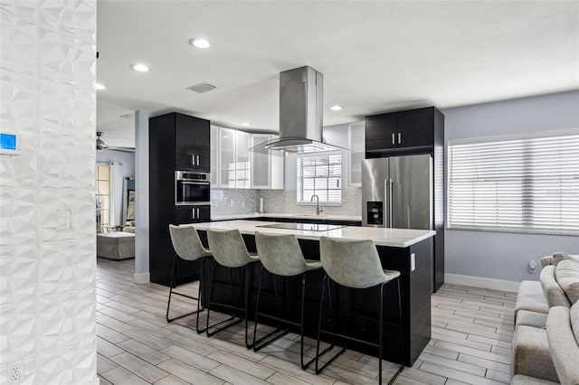 kitchen featuring appliances with stainless steel finishes, island range hood, light wood-type flooring, and a breakfast bar