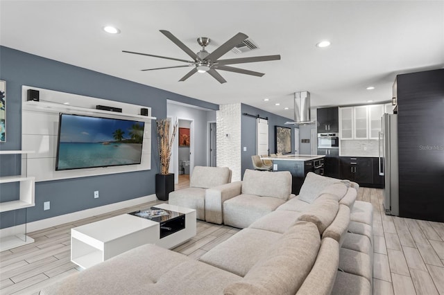 living room featuring light wood-type flooring, ceiling fan, and a barn door