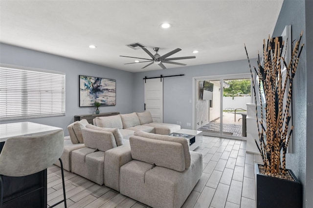 living room with ceiling fan, light wood-type flooring, and a barn door