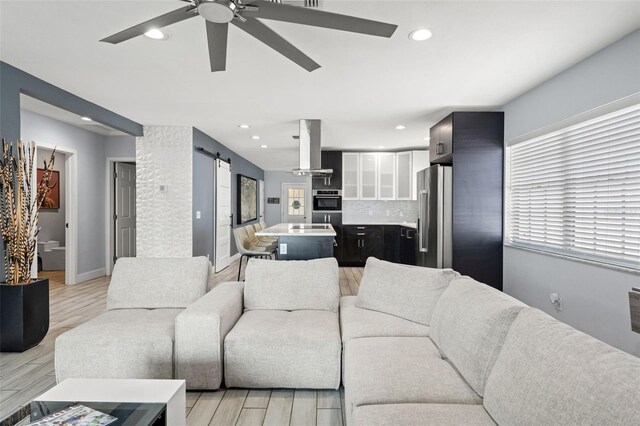 living room with ceiling fan, light hardwood / wood-style flooring, and a barn door