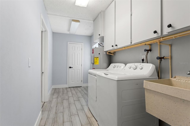 washroom featuring sink, a textured ceiling, washer and clothes dryer, cabinets, and electric water heater