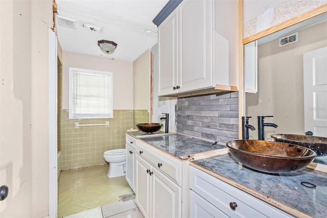 kitchen with light tile patterned flooring, backsplash, sink, tile walls, and white cabinetry