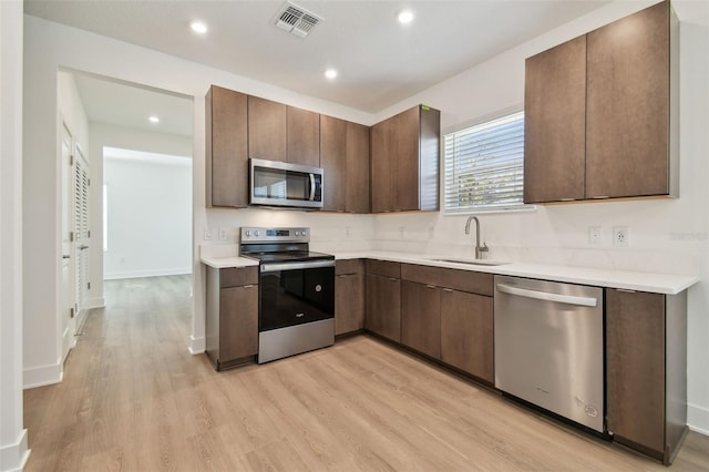 kitchen with dark brown cabinetry, appliances with stainless steel finishes, light countertops, light wood-style floors, and a sink