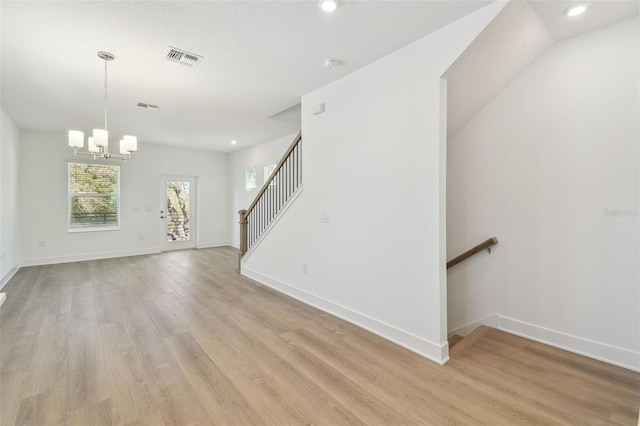 unfurnished living room featuring light wood finished floors, visible vents, stairway, an inviting chandelier, and baseboards