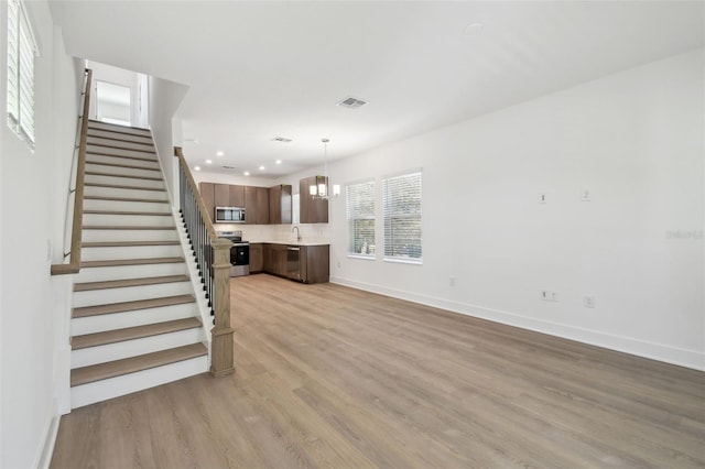 unfurnished living room with baseboards, stairway, light wood-style flooring, and a notable chandelier