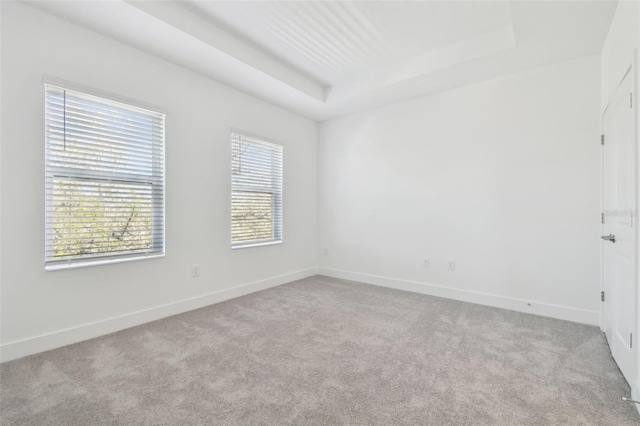 carpeted empty room with baseboards and a raised ceiling