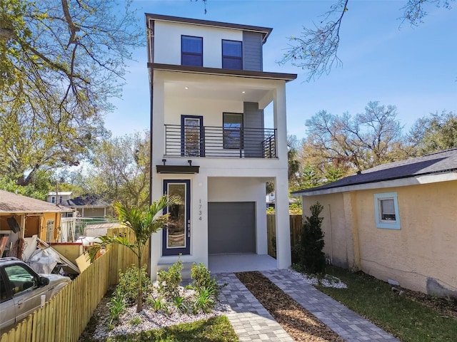 contemporary home featuring a garage, fence, a balcony, and stucco siding