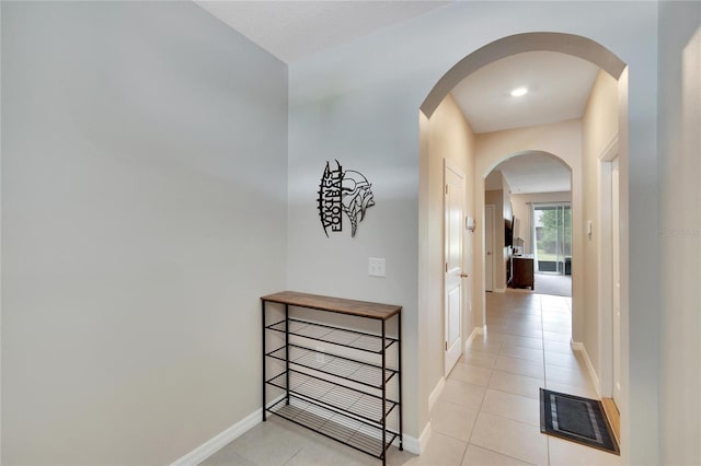 corridor featuring baseboards, visible vents, arched walkways, and light tile patterned flooring