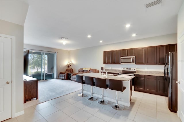 kitchen with electric stove, fridge, light colored carpet, a breakfast bar, and a center island with sink