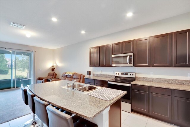 kitchen featuring stainless steel appliances, sink, an island with sink, light tile patterned flooring, and a breakfast bar