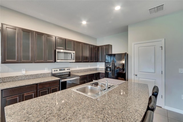 kitchen with a breakfast bar, appliances with stainless steel finishes, light stone countertops, light tile patterned floors, and sink