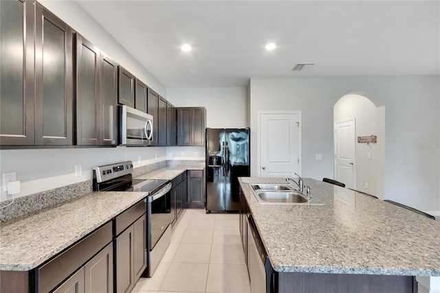 kitchen with appliances with stainless steel finishes, sink, light stone counters, an island with sink, and light tile patterned floors