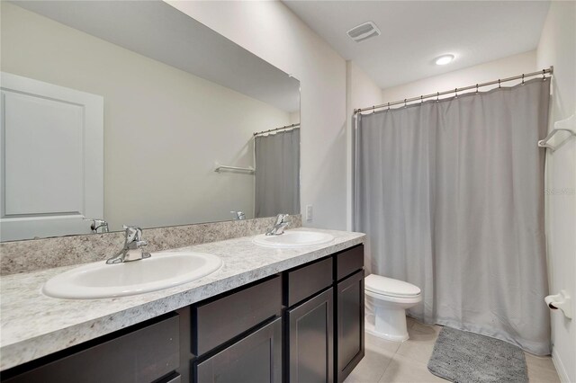 bathroom featuring toilet, dual vanity, and tile patterned floors