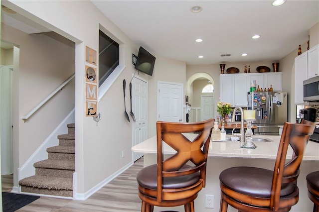 kitchen featuring appliances with stainless steel finishes, white cabinets, a kitchen breakfast bar, light wood-type flooring, and sink