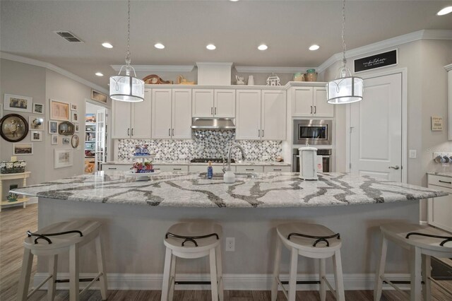 kitchen featuring a spacious island, white cabinetry, hanging light fixtures, and stainless steel microwave