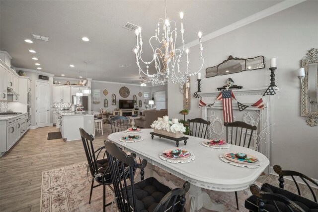 dining room with light hardwood / wood-style floors, ornamental molding, and an inviting chandelier