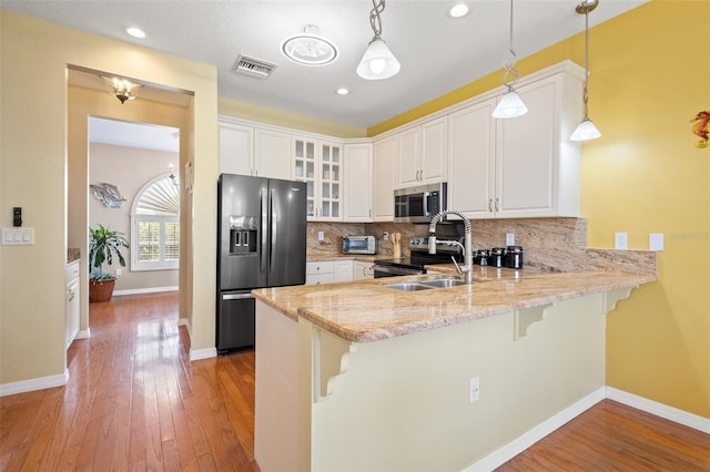 kitchen with appliances with stainless steel finishes, light hardwood / wood-style flooring, tasteful backsplash, pendant lighting, and kitchen peninsula