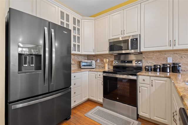 kitchen featuring stainless steel appliances, light hardwood / wood-style floors, decorative backsplash, white cabinetry, and light stone counters