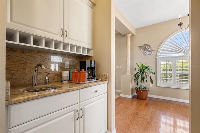 kitchen with light wood-type flooring, tasteful backsplash, white cabinets, light stone countertops, and sink