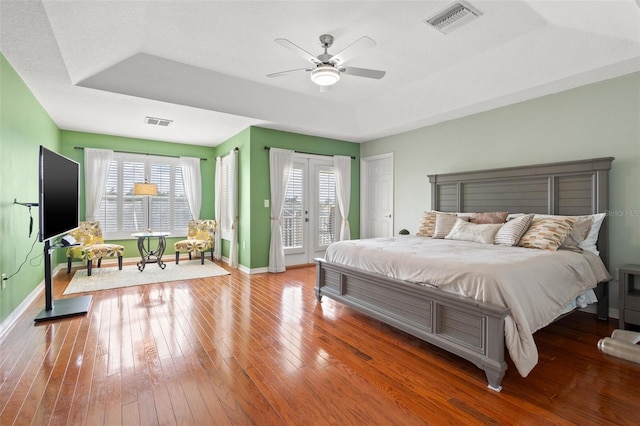 bedroom with ceiling fan, a raised ceiling, access to outside, french doors, and hardwood / wood-style flooring