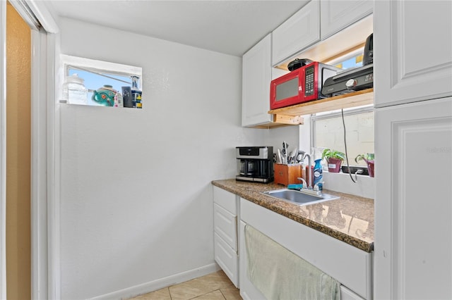 kitchen with white cabinets, light tile patterned flooring, dark stone countertops, and sink